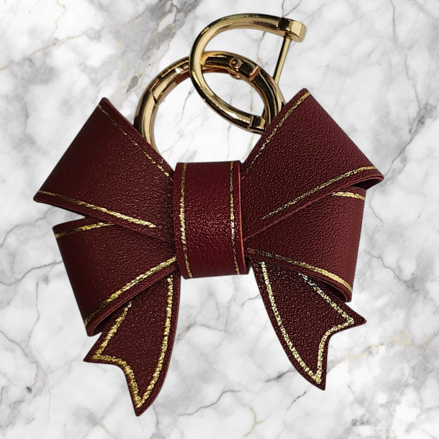 A luxury deep red faux leather bow trimmed in gold charm pendant that can be used as a charm for your tumbler, tumbler straw, purse, bag, keychain, backpack, or cellphone. Pictured with extra gold keyring.