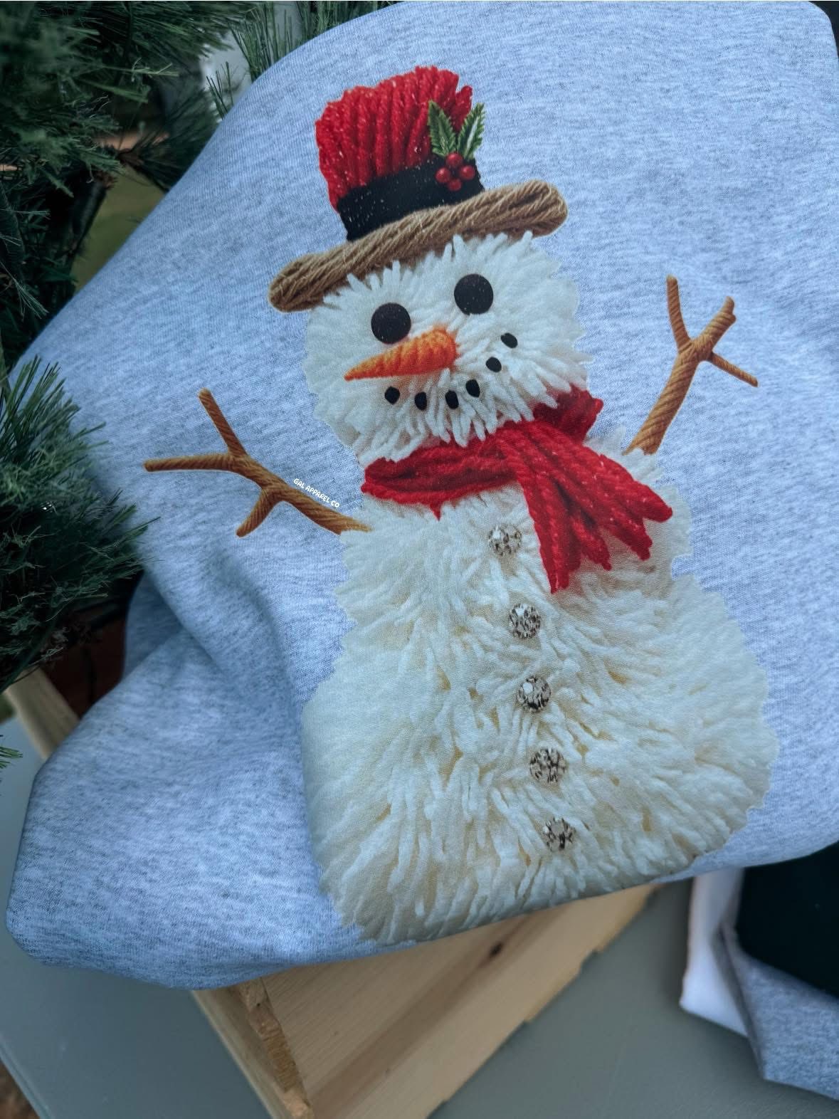 Snowman faux yarn design on gray Christmas t-shirt and sweatshirt with red scarf and top hat, cozy holiday graphic apparel.